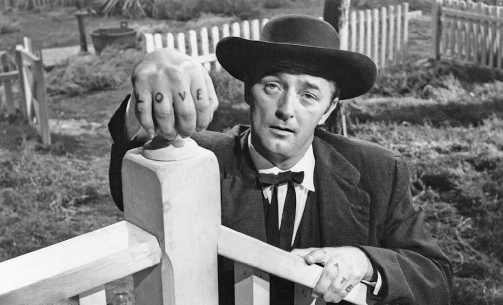 Black-and-white still from The Night of the Hunter showing a preacher-like man in a dark hat with LOVE tattooed across his fingers.
